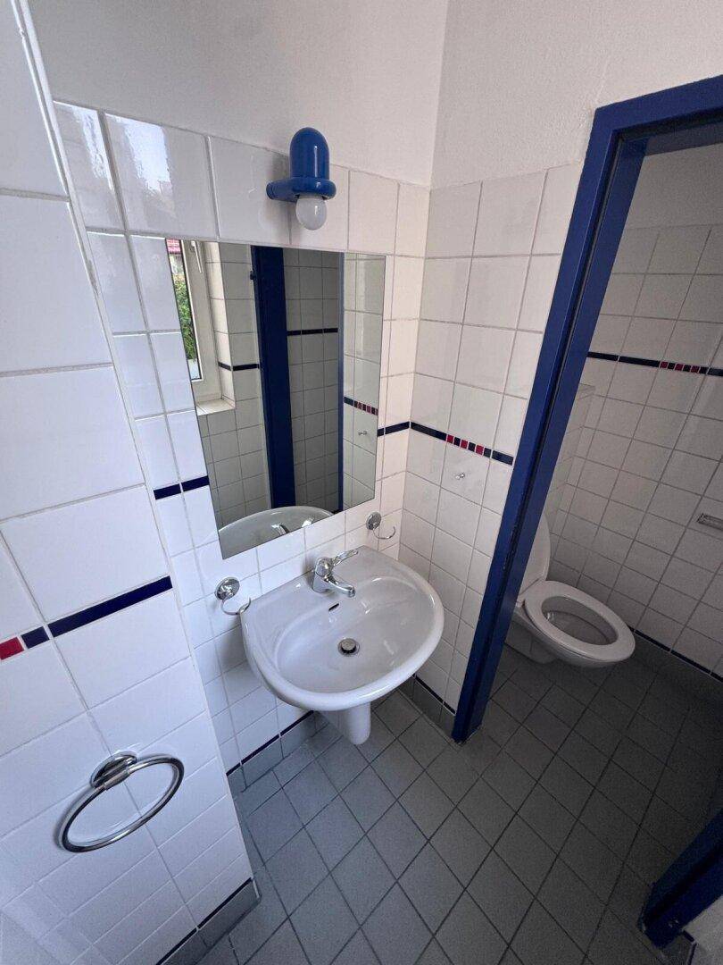 Kleines Badezimmer mit Waschbecken, Spiegel und WC, ausgestattet mit weißen und grauen Fliesen.