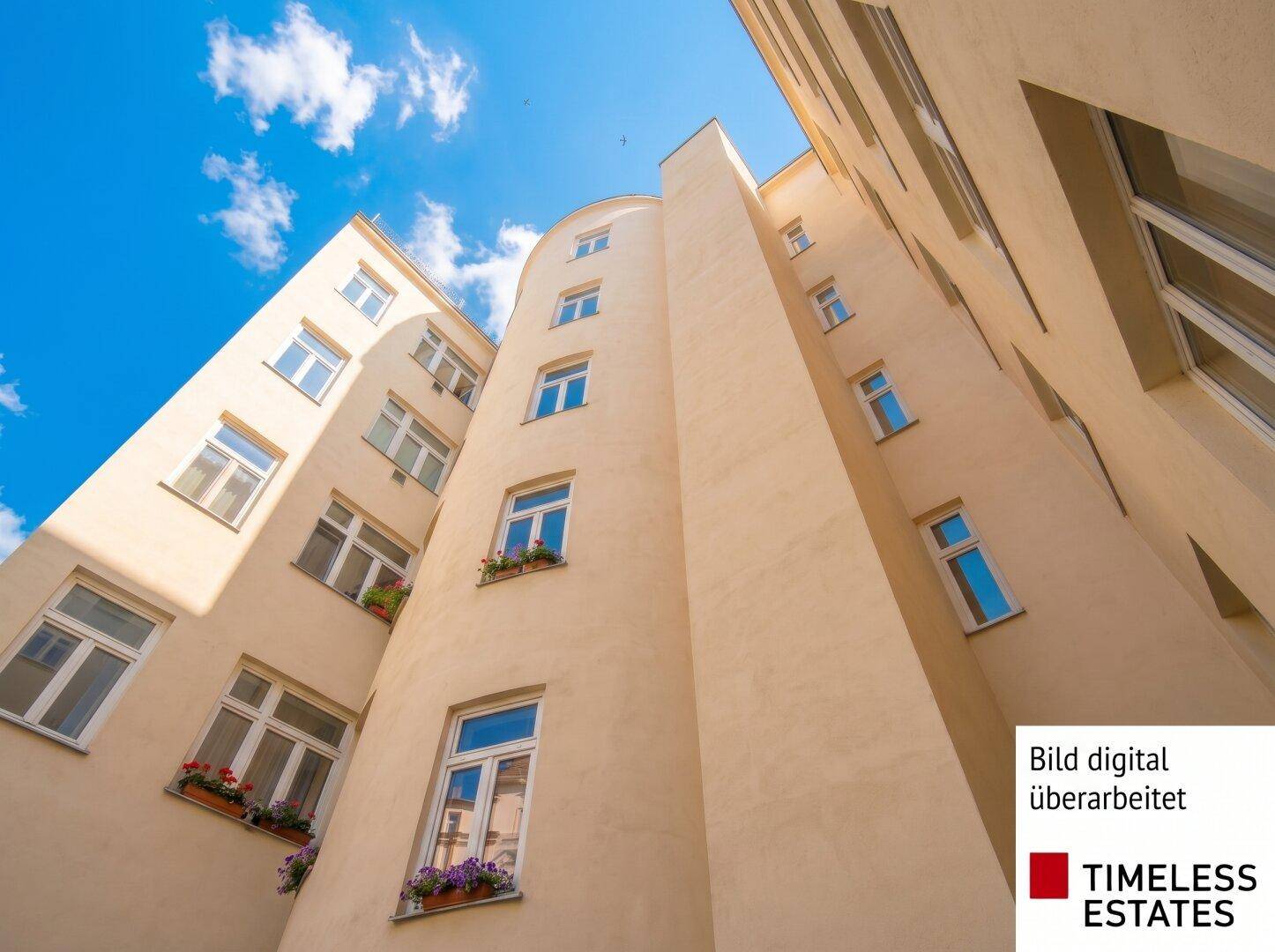 Gebäudeansicht von unten mit einer geschwungenen, hellen Fassade und vielen Fenstern unter blauem Himmel.