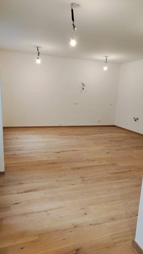 Geräumiger, unmöblierter Raum mit hellem Holzparkettboden und weißen Wänden.