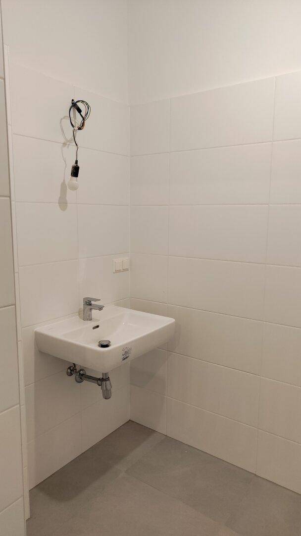 Modern gefliestes Gäste-WC mit einem einzelnen Waschbecken und weißen Wänden.