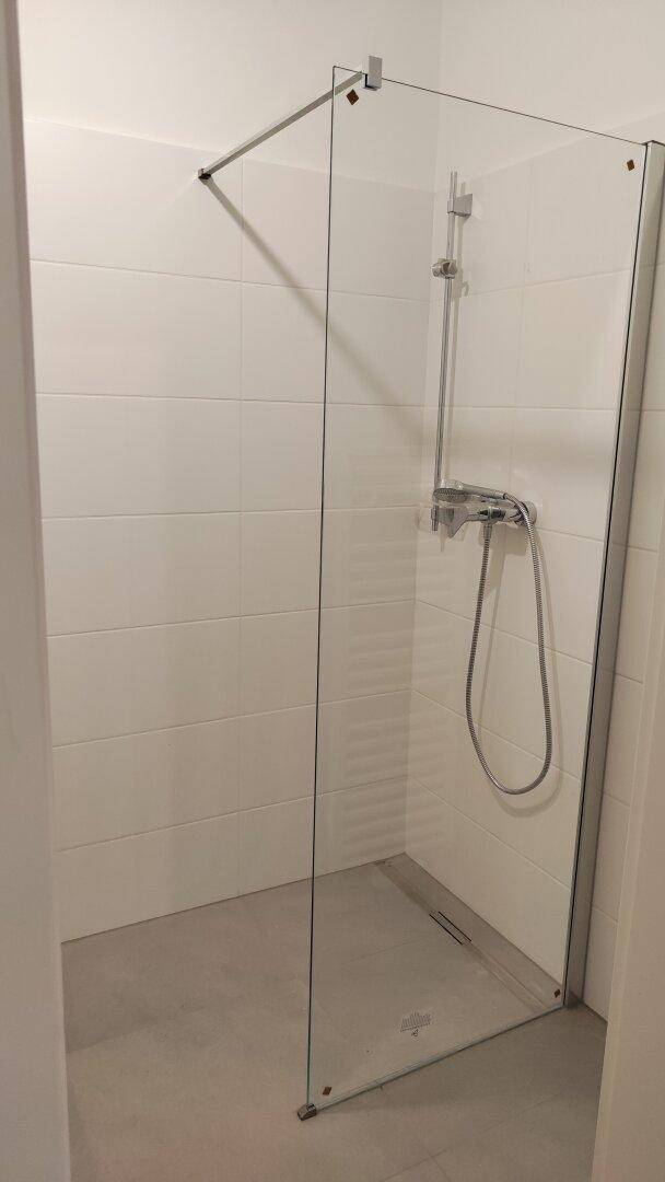 Modernes Badezimmer mit begehbarer Dusche und weißen Fliesen an den Wänden.