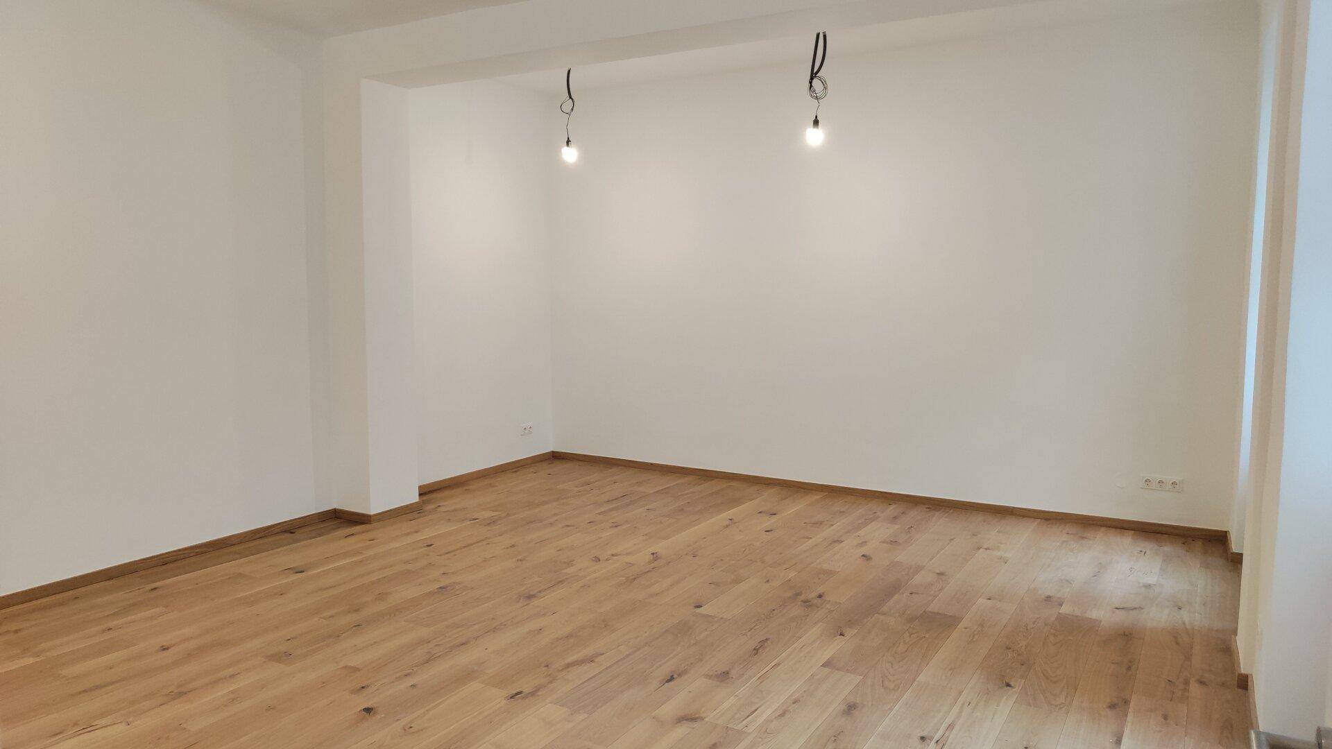 Geräumiges, leeres Zimmer mit hellem Holzboden und weißen Wänden, bereit zur Einrichtung.