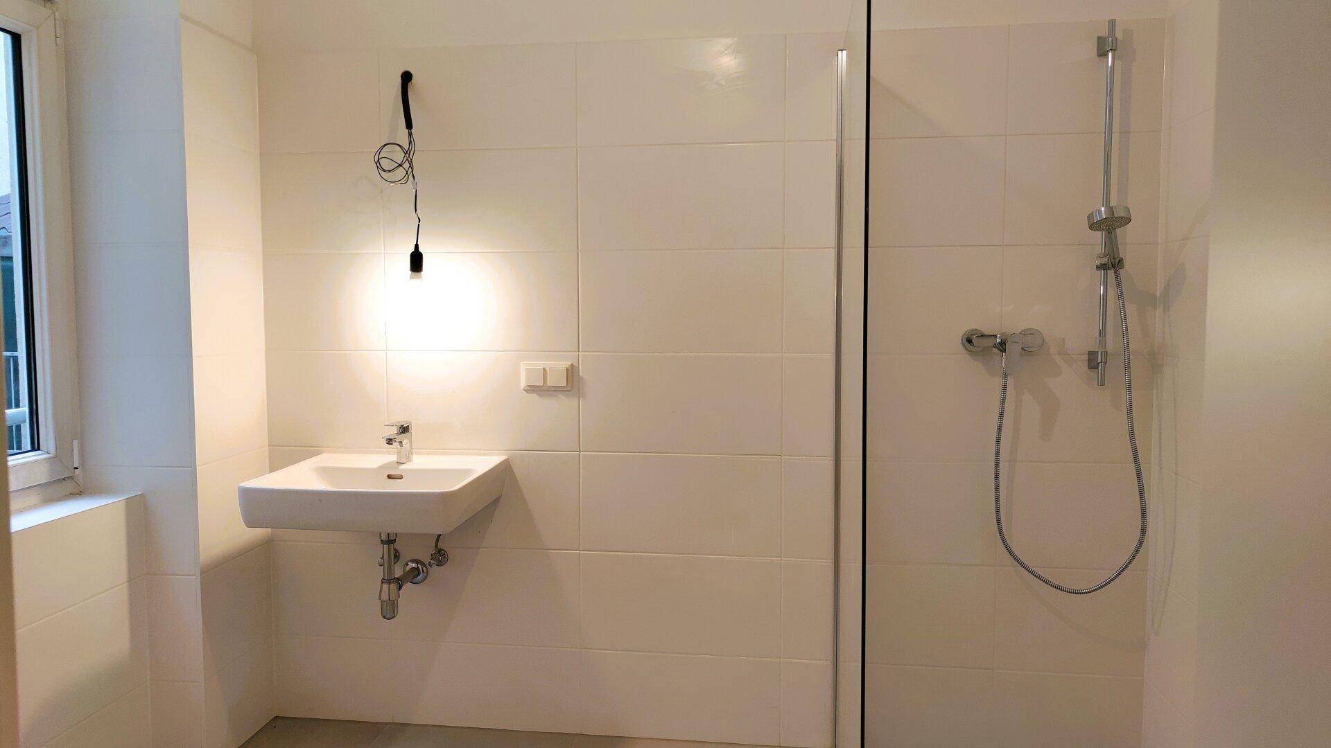 Modernes Badezimmer mit weißen Fliesen, Waschbecken und einer Duschkabine mit Glaswand.