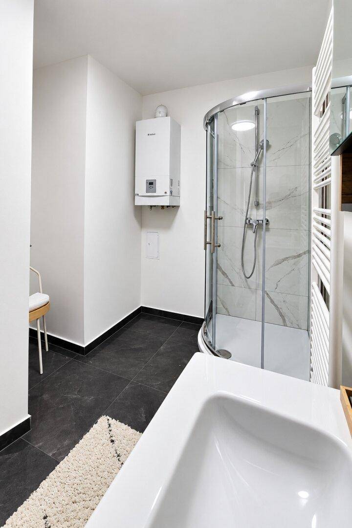 Modernes Badezimmer mit Duschkabine, dunklen Fliesen und Heizkörper.