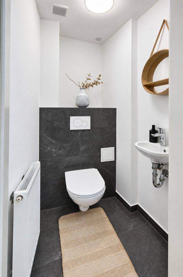 Kleines Gäste-WC mit Wand-WC, Waschbecken und dunklen Fliesen.