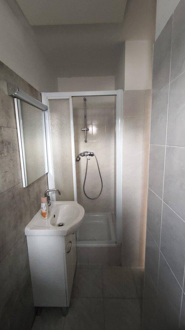 Modernes Badezimmer mit grauen Fliesen, Waschtisch und Duschkabine.