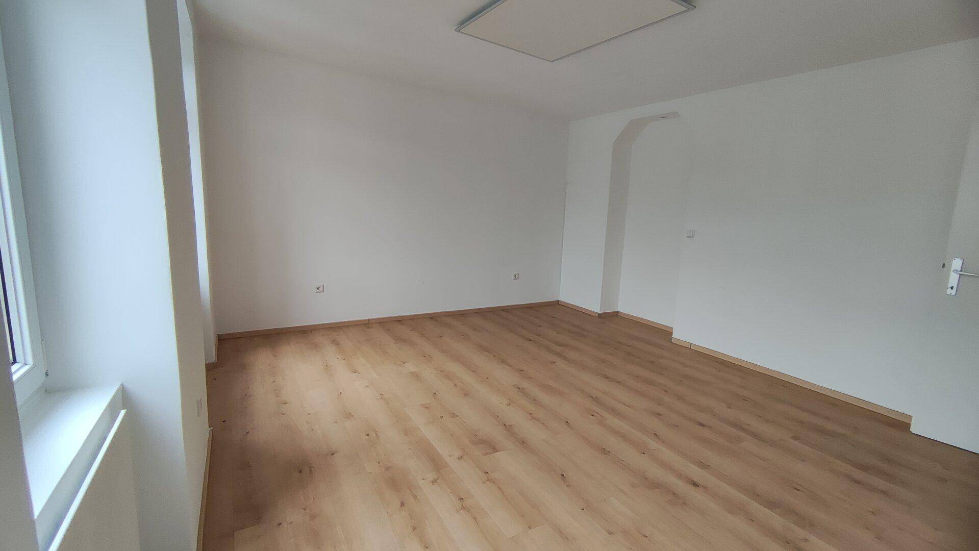 Leeres Zimmer mit Laminatboden und weiß gestrichenen Wänden, bietet vielseitige Nutzungsmöglichkeiten.