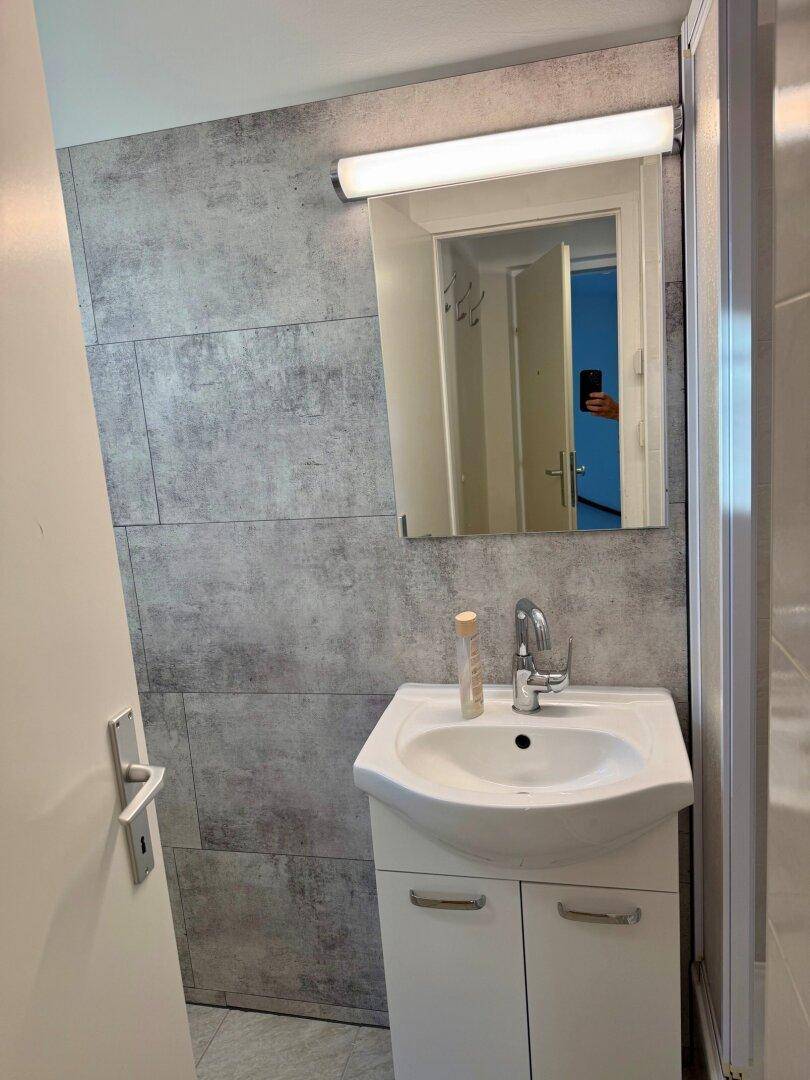 Modernes Badezimmer mit Einzelwaschbecken, Spiegelschrank und grauen Fliesen an der Wand.