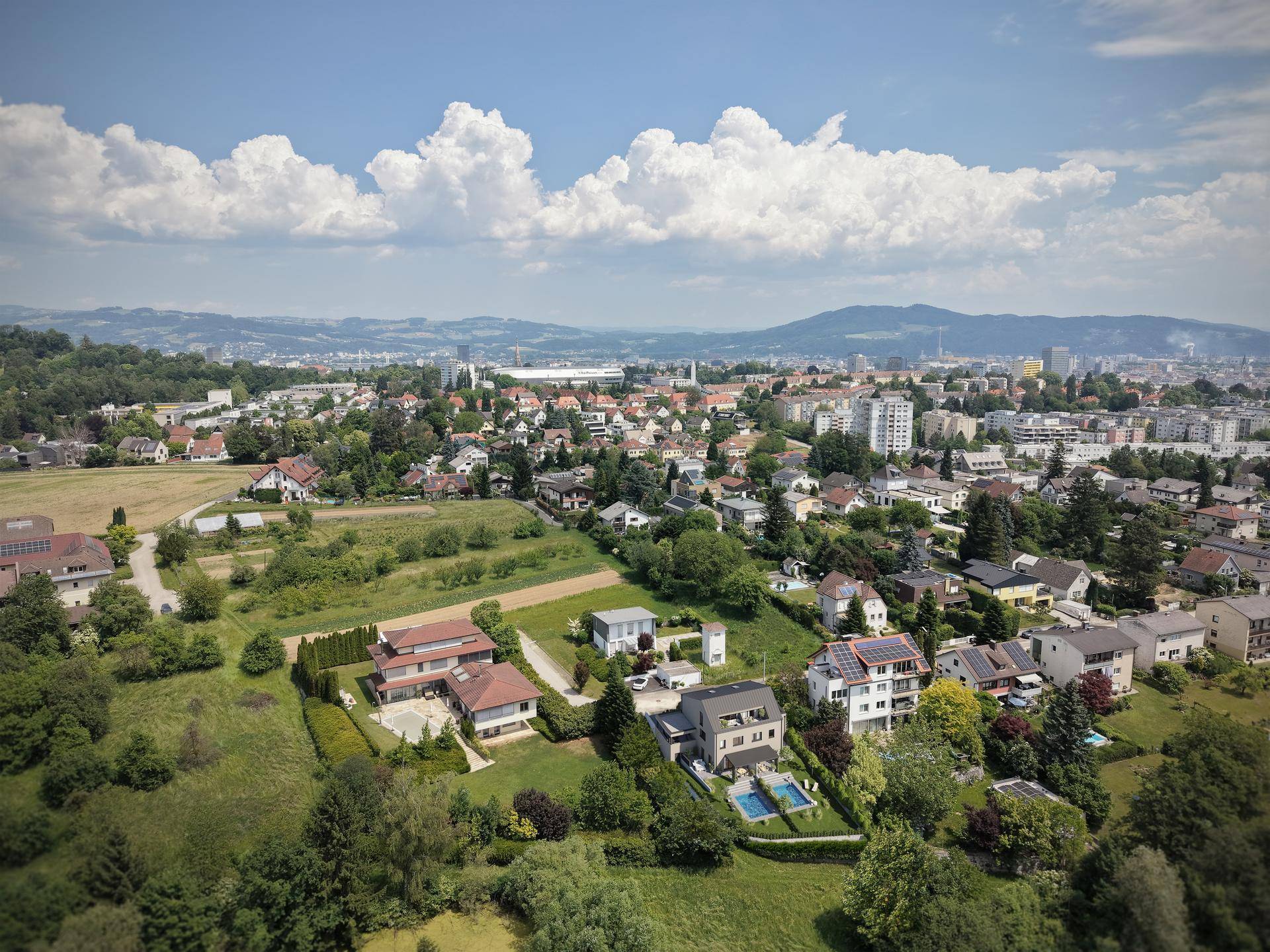 Weitläufige Luftaufnahme einer Wohnsiedlung mit viel Grün und Stadtblick im Hintergrund.