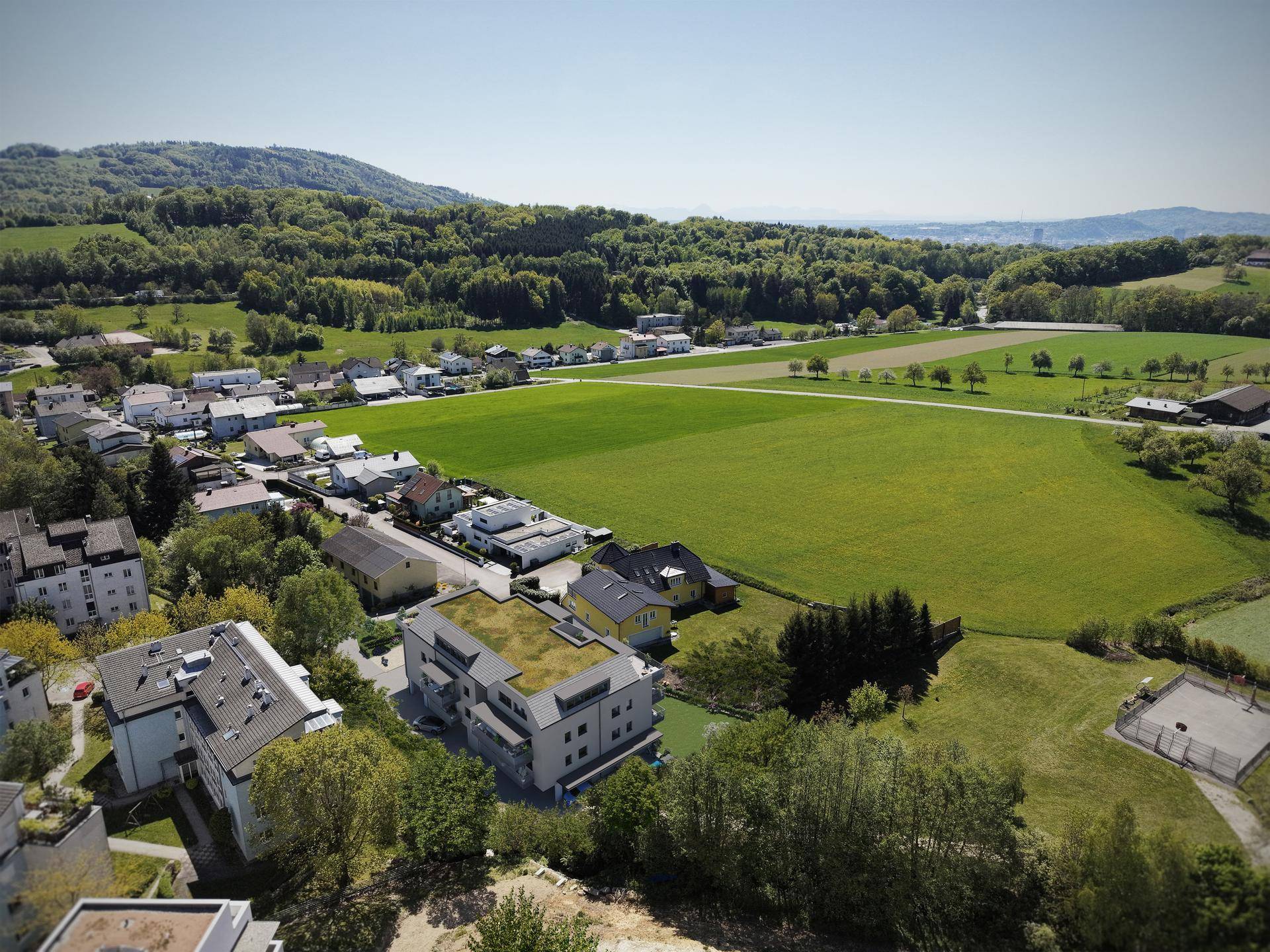 Weitläufige Luftaufnahme der Wohnsiedlung eingebettet in grüne Landschaft und Wälder.