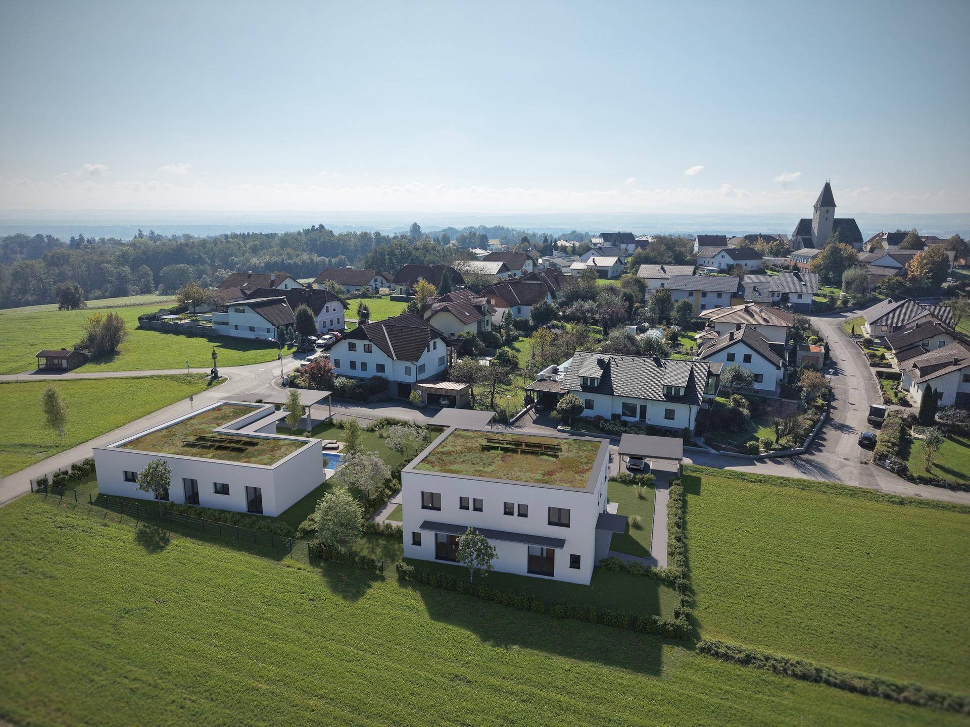 Weitläufige Luftaufnahme von zwei modernen Häusern am Rande eines Dorfes mit Kirche.