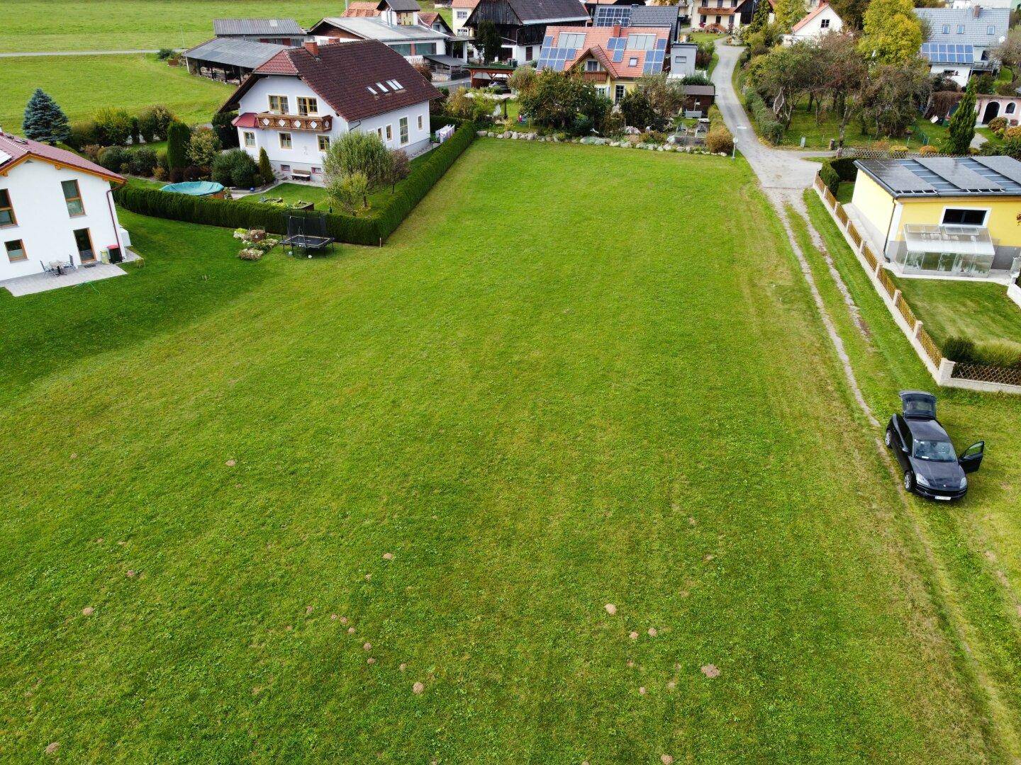 Luftaufnahme eines weitläufigen grünen Grundstücks mit angrenzenden Wohnhäusern und ländlicher Umgebung.