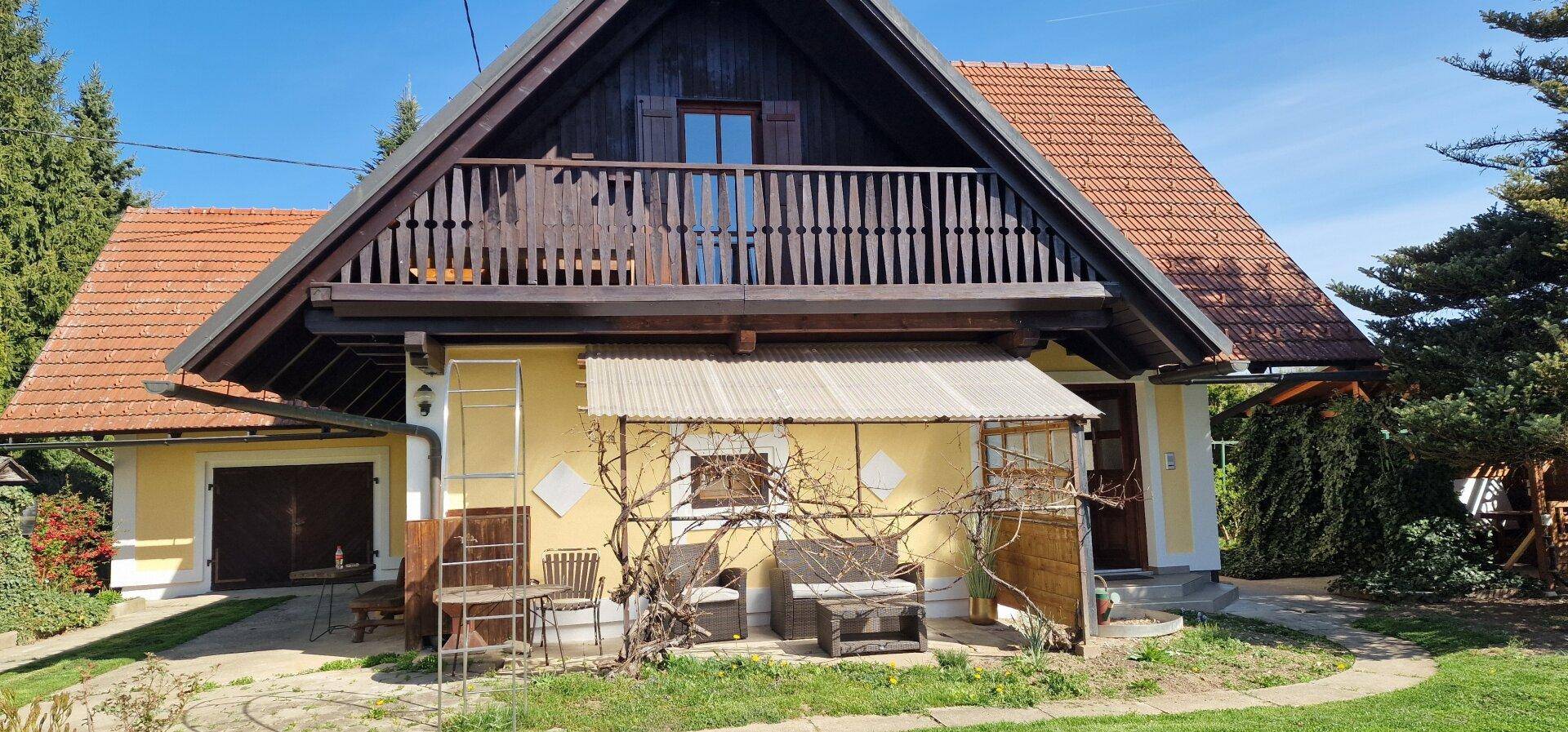 Charmantes Landhaus mit gelber Fassade, Holzbalkon und überdachtem Eingangsbereich.
