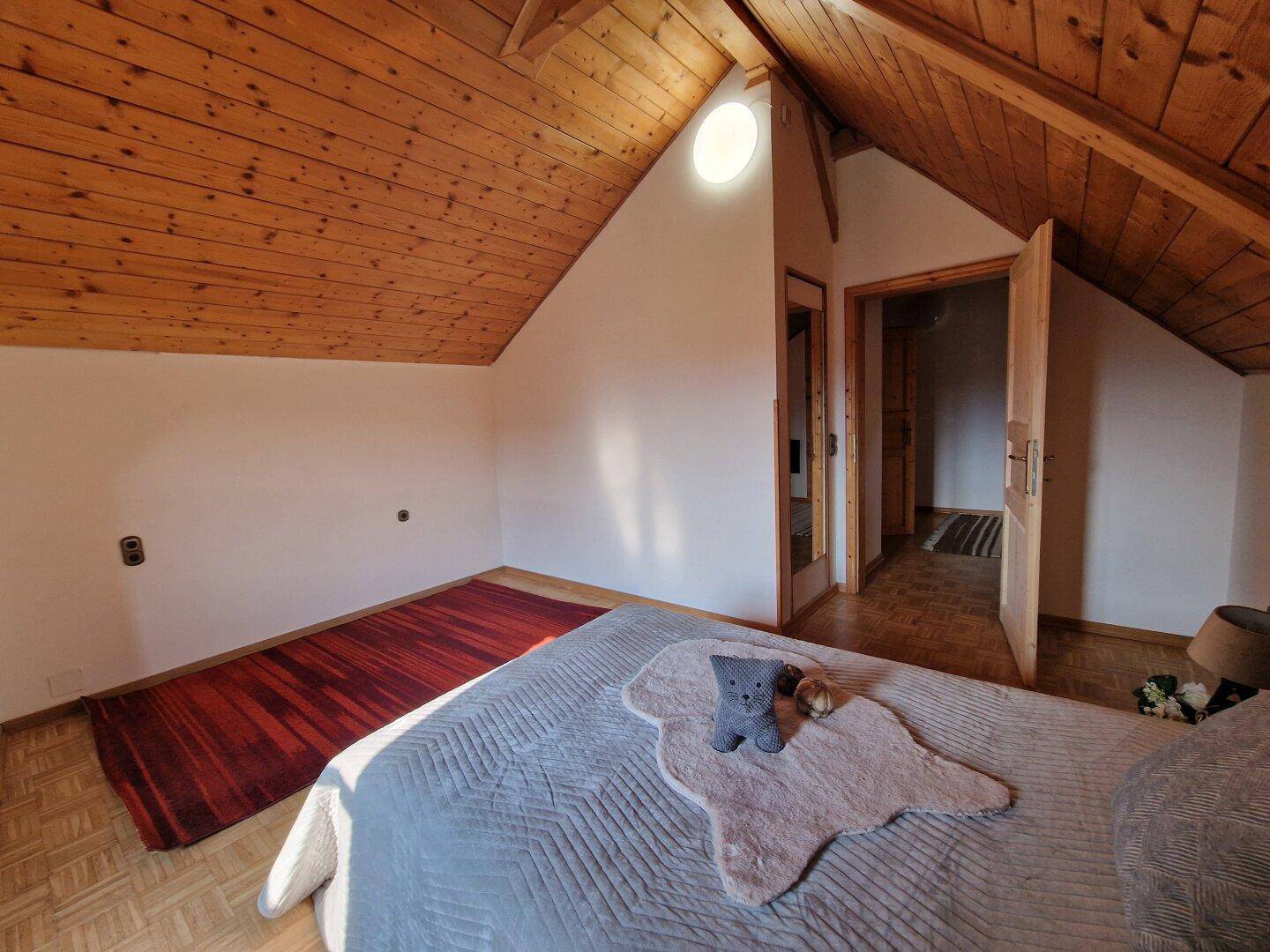Helles Schlafzimmer im Dachgeschoss mit Holzbalkendecke, Parkettboden und runder Dachluke.