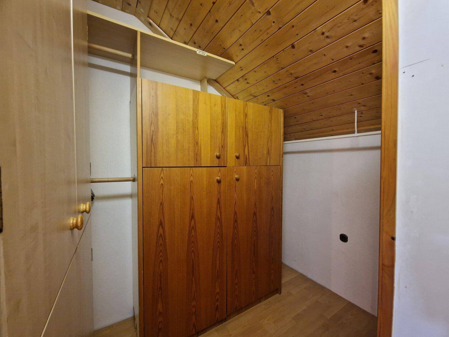 Praktischer begehbarer Kleiderschrank im Dachgeschoss mit Holzschränken und Stauraum.