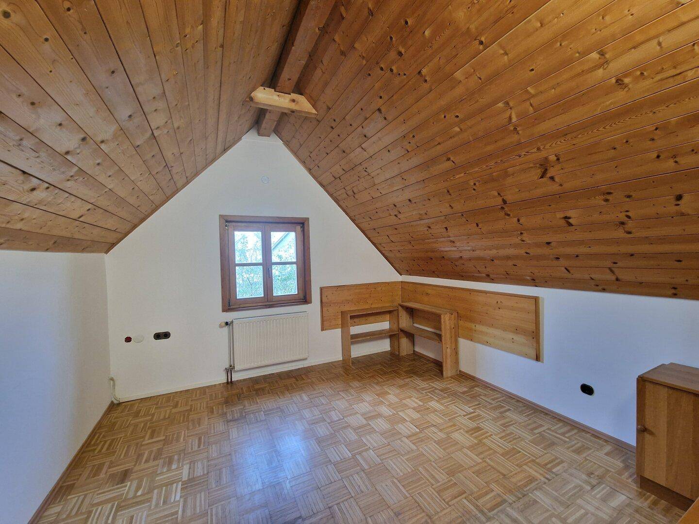 Helles Schlafzimmer im Dachgeschoss mit Holzbalkendecke, Parkettboden und Fenster mit Ausblick.