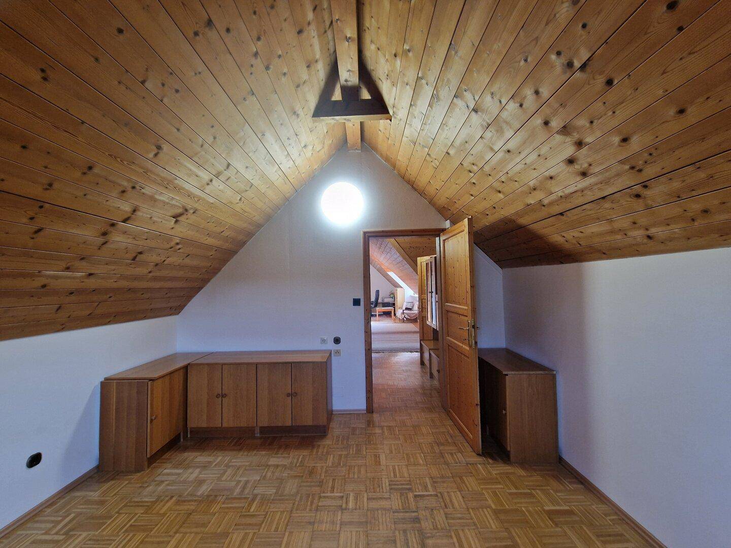 Vielseitiger Dachbodenraum mit Holzbalkendecke, Parkettboden und runder Dachluke.