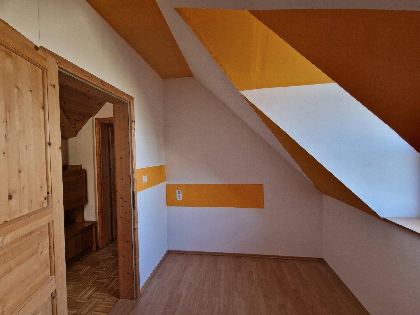 Kleines Zimmer im Dachgeschoss mit schrägen Wänden, Laminatboden und farbigen Akzenten.