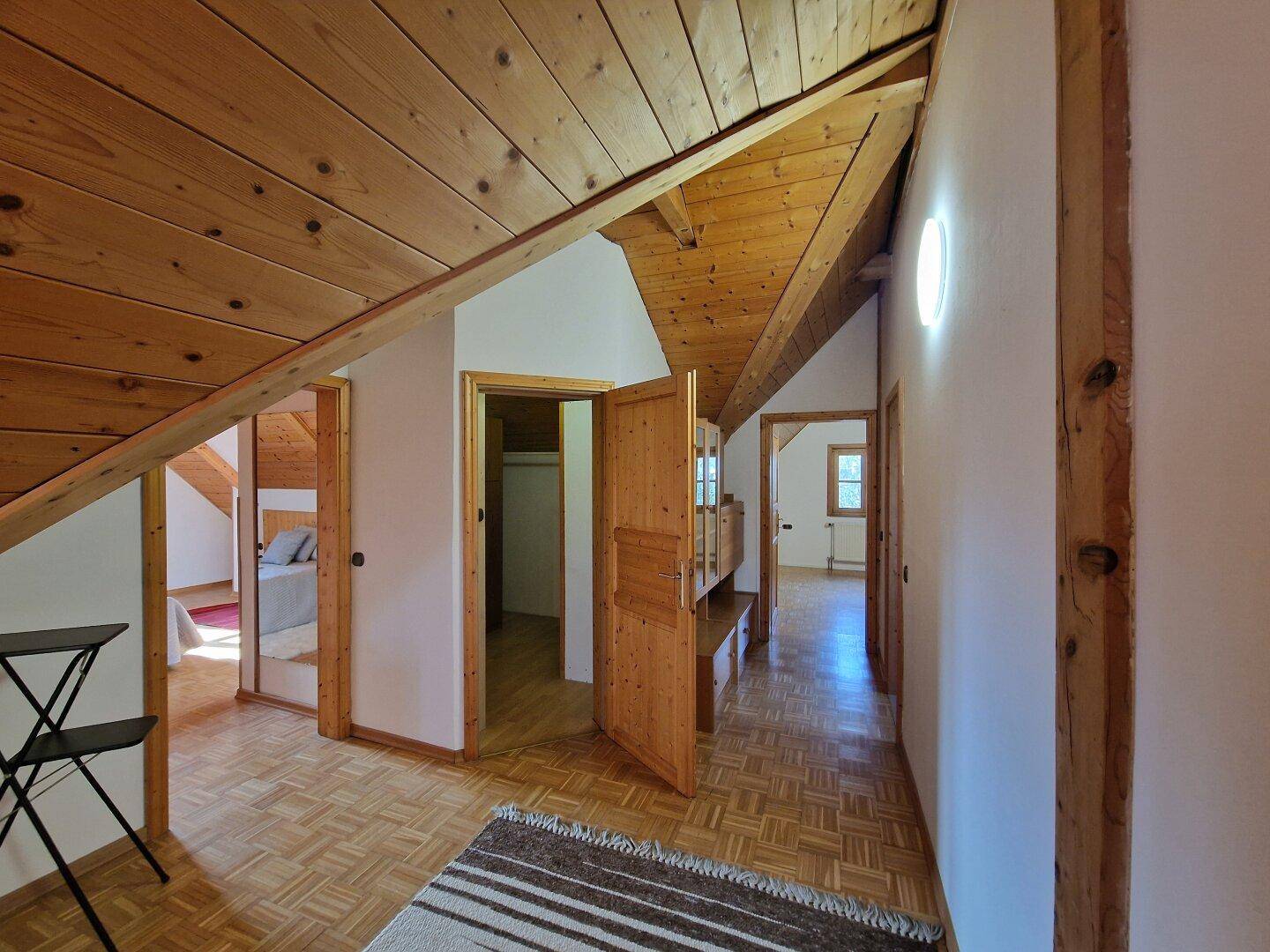 Langer Flur im Dachgeschoss mit Holzbalkendecke, Parkettboden und Zugang zu mehreren Zimmern.