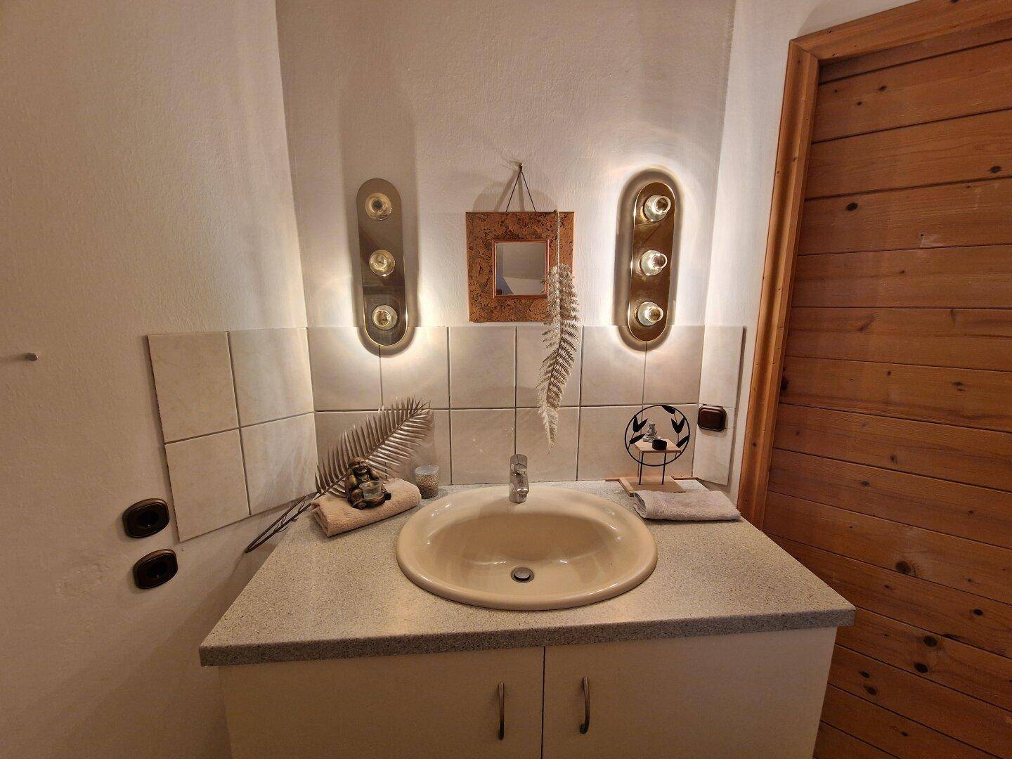 Detailansicht des Waschbeckens im Badezimmer mit Spiegelschrank und Wandleuchten.