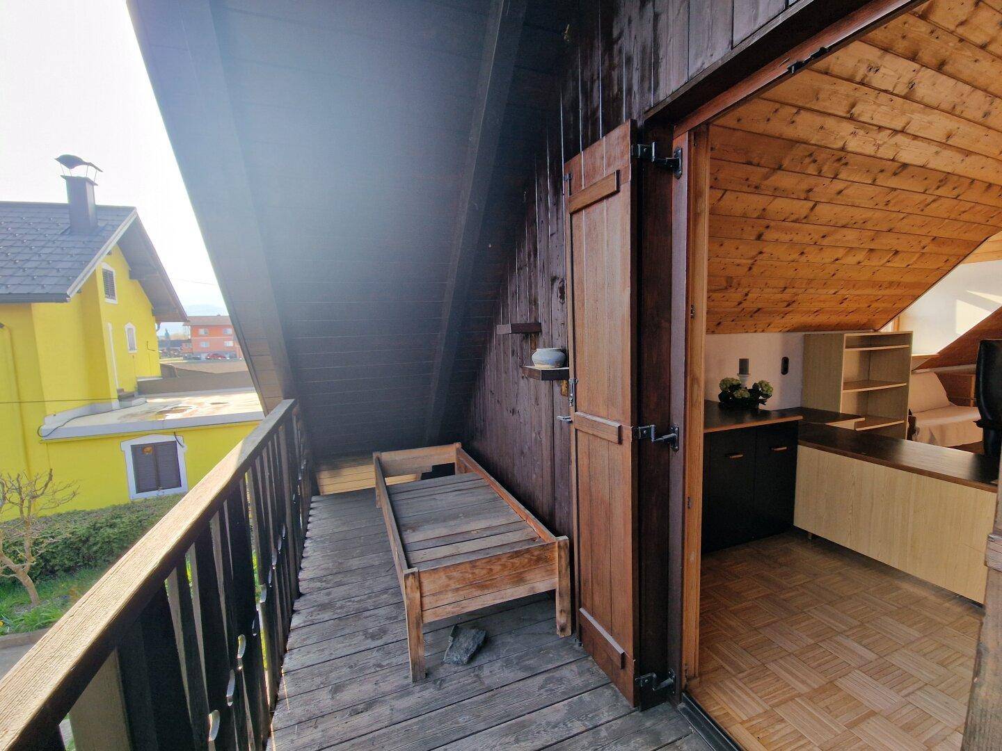 Geräumiger Holzbalkon mit Blick auf die Umgebung, zugänglich von einem Zimmer im Dachgeschoss.
