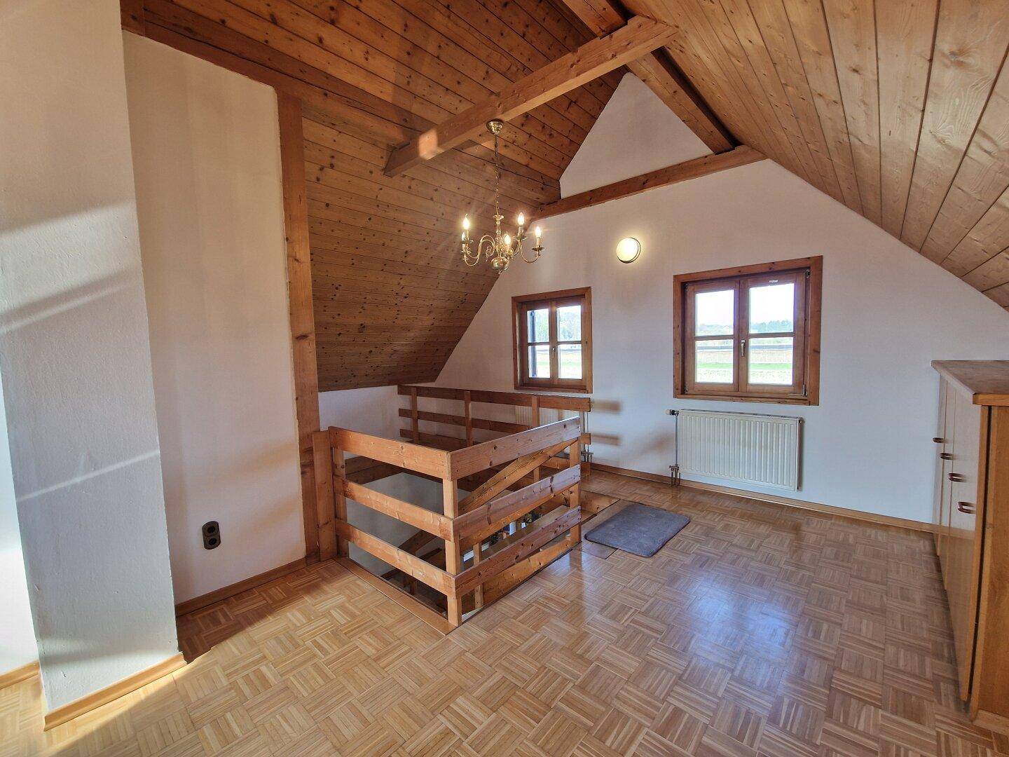 Geräumiger Dachbodenraum mit Holzbalkendecke, Parkettboden und Fenstern mit Blick ins Grüne.