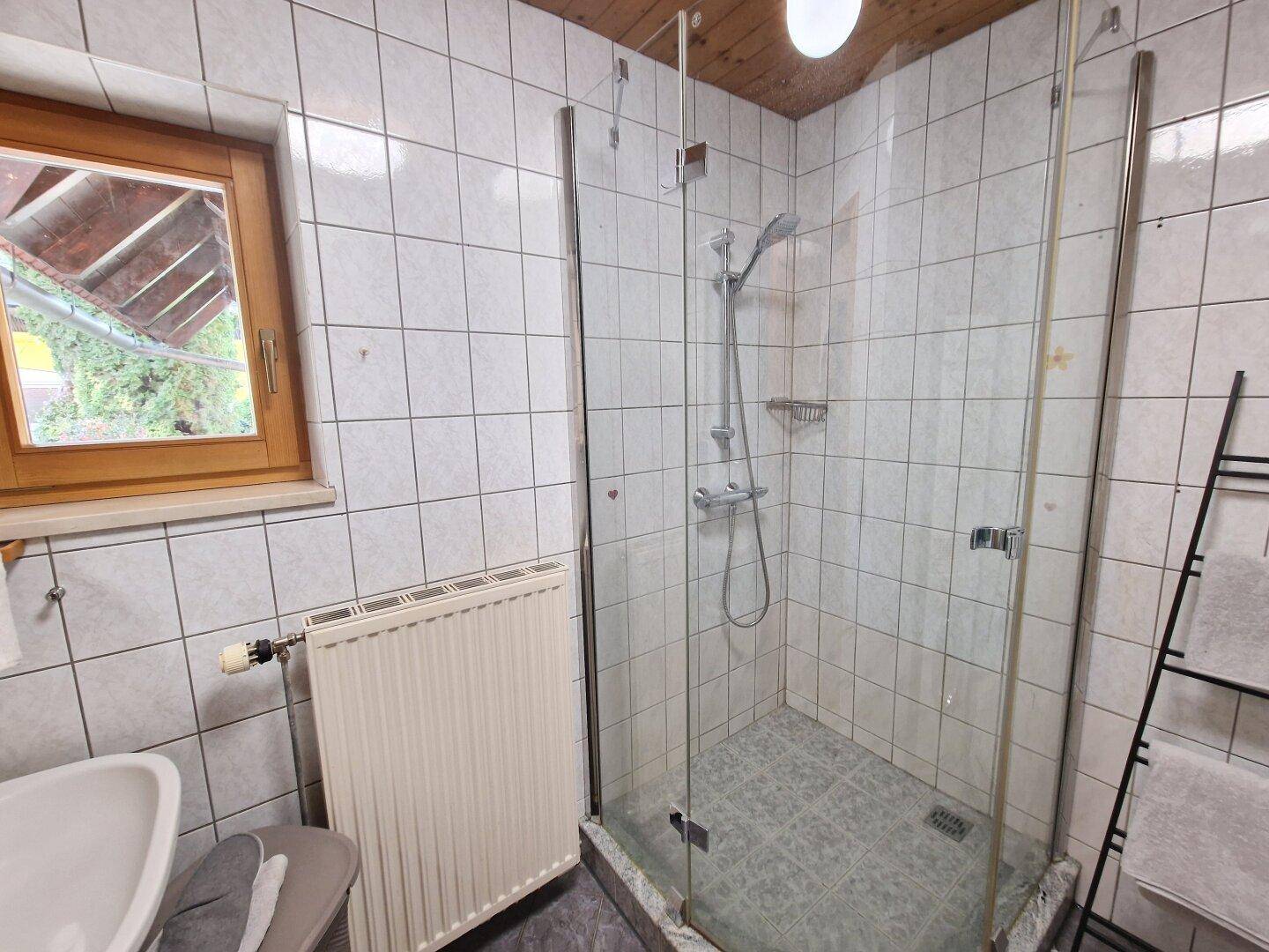 Badezimmer mit Duschkabine, Fliesen an Wänden und Boden sowie einem Fenster.
