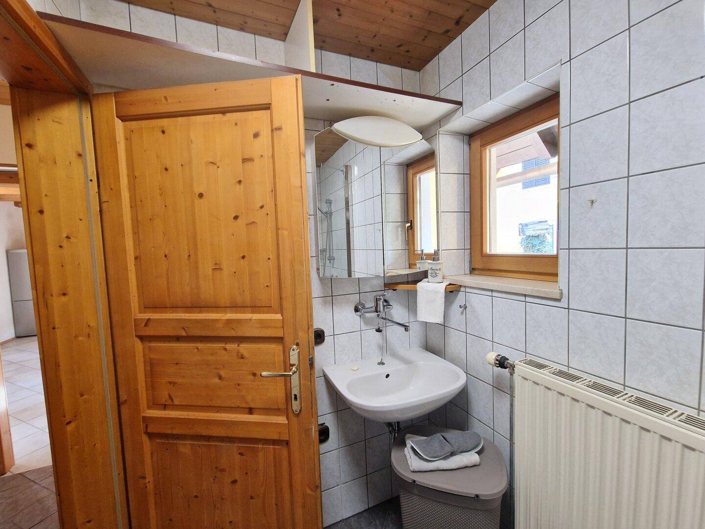 Helles Badezimmer mit Waschbecken, Spiegelschrank und Fenster, das Tageslicht hereinlässt.