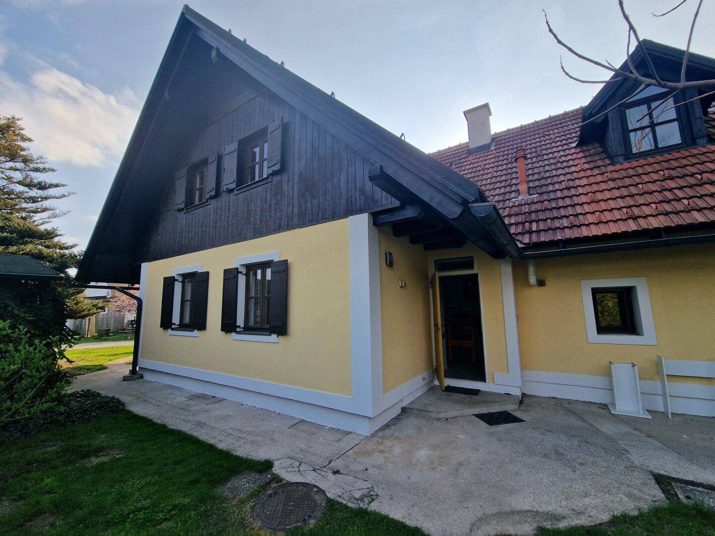 Seitenansicht eines traditionellen Hauses mit gelber Fassade, dunklen Fensterläden und rotem Ziegeldach.