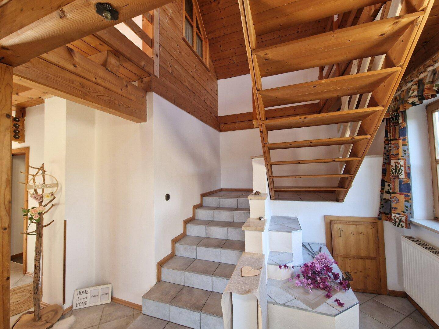 Treppenhaus mit Holztreppe, Fliesenstufen und sichtbaren Holzbalken, die den rustikalen Stil betonen.