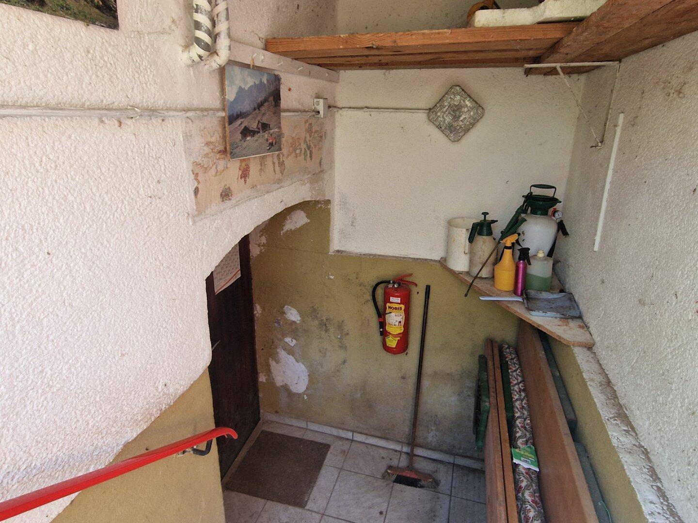 Eingangsbereich im Keller mit Fliesenboden, Feuerlöscher und Reinigungsutensilien.
