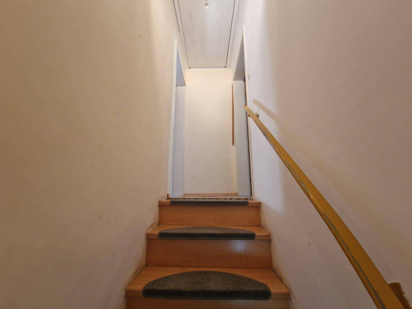 Schmale Holztreppe mit Teppichstufen, führt zu den oberen Räumen.