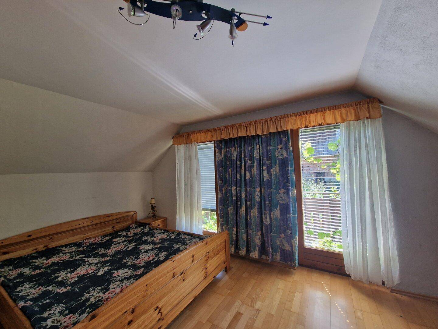 Schlafzimmer im Dachgeschoss mit Holzboden, Bett und Fenster mit Blick ins Grüne.