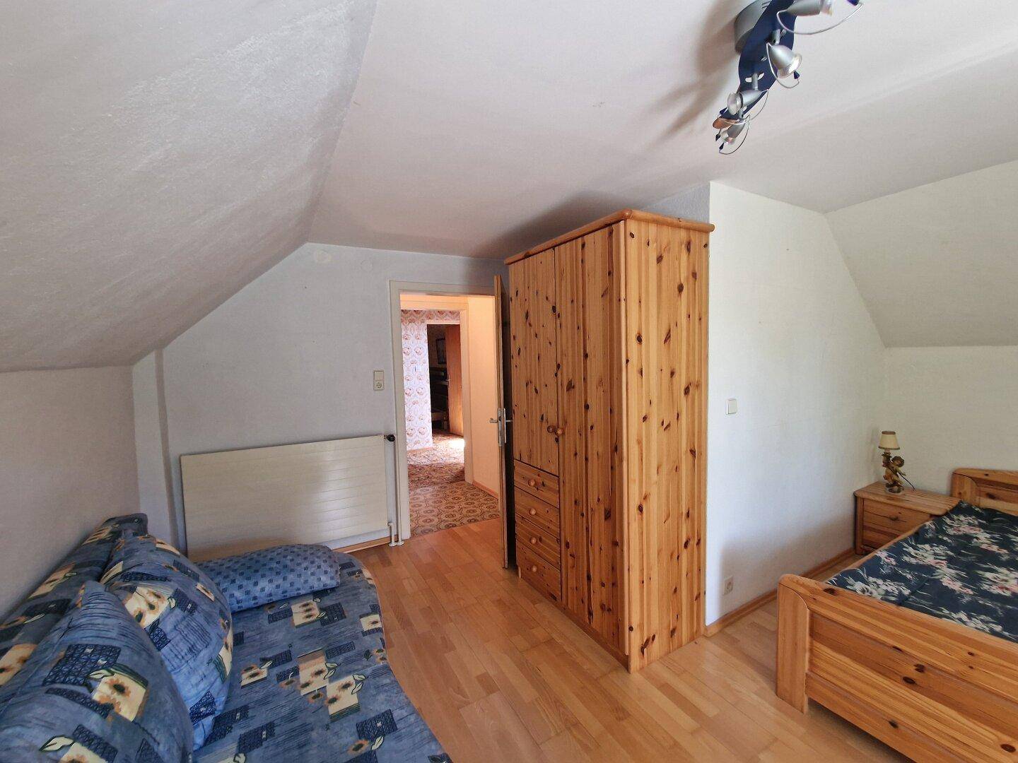 Dachgeschoss-Schlafzimmer mit Holzboden, Kleiderschrank und Zugang zu einem weiteren Raum.
