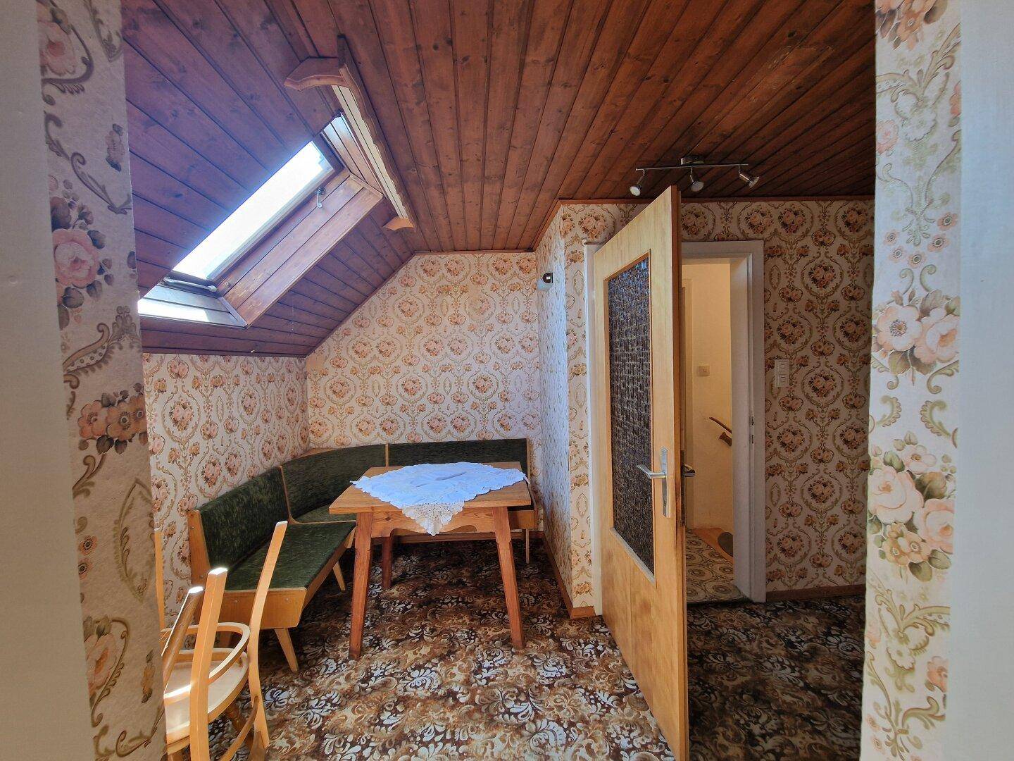 Gemütlicher Essbereich im Dachgeschoss mit Eckbank, Holztisch und Dachfenster.