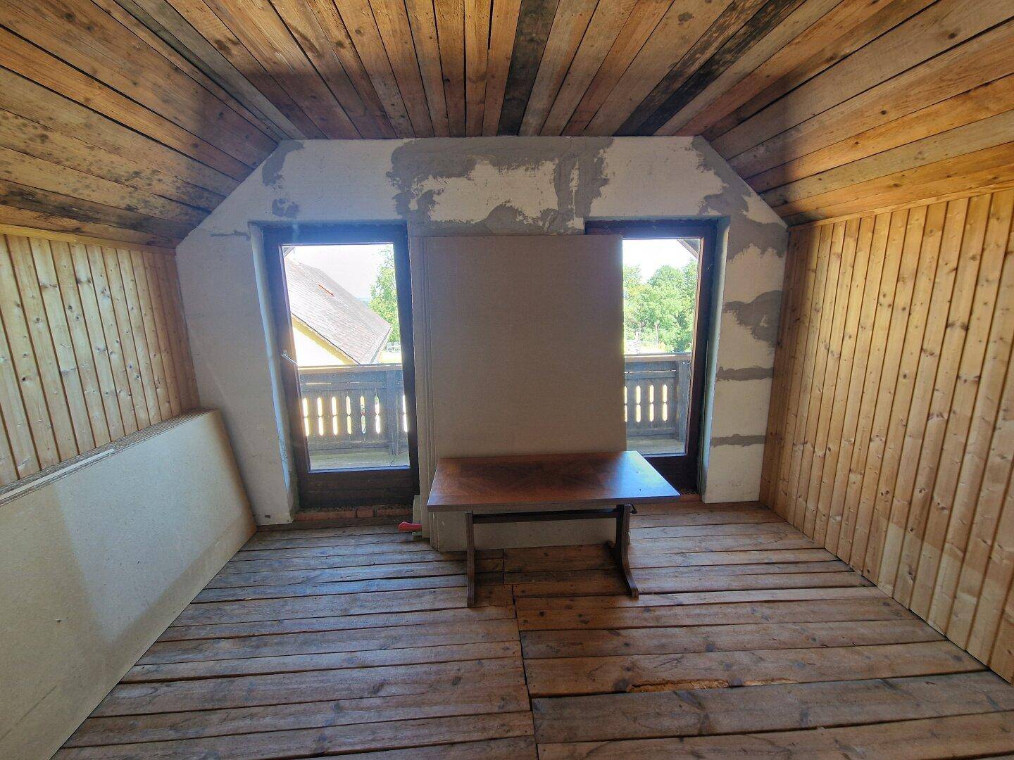 Unfertiger Dachgeschossraum mit Holzverkleidung, Holzboden und Fenstern.