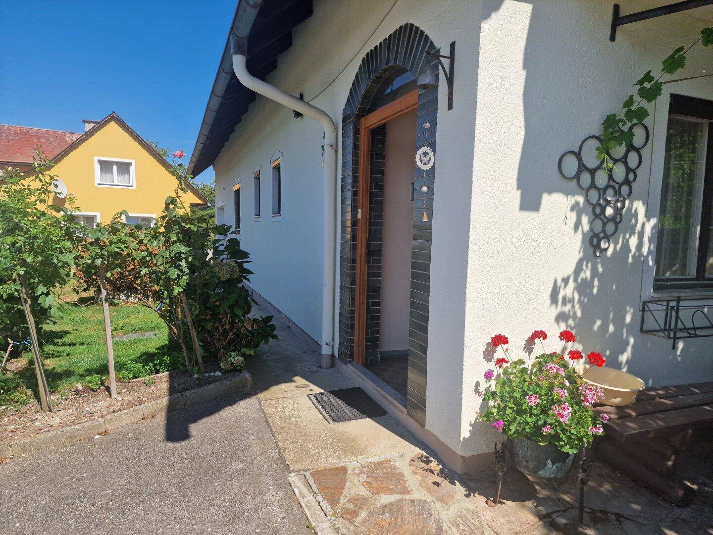 Seitenansicht des Hauses mit Eingangsbereich, gepflegtem Vorgarten und sonniger Lage.