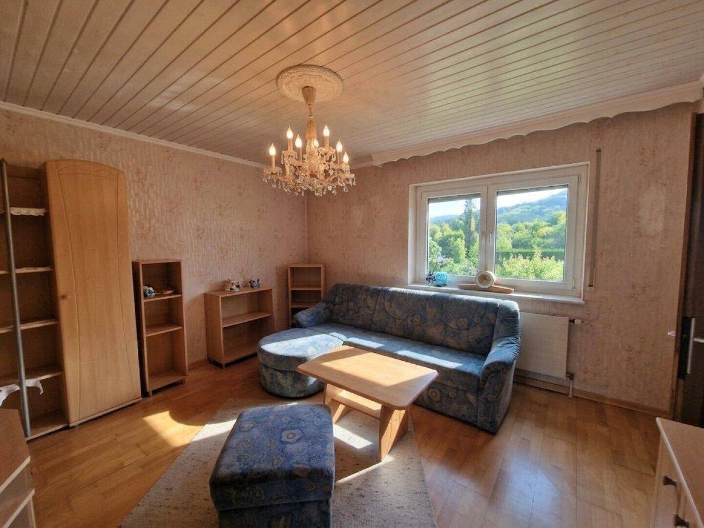 Helles Wohnzimmer mit Holzboden, Sofa, Schränken und Blick ins Grüne.
