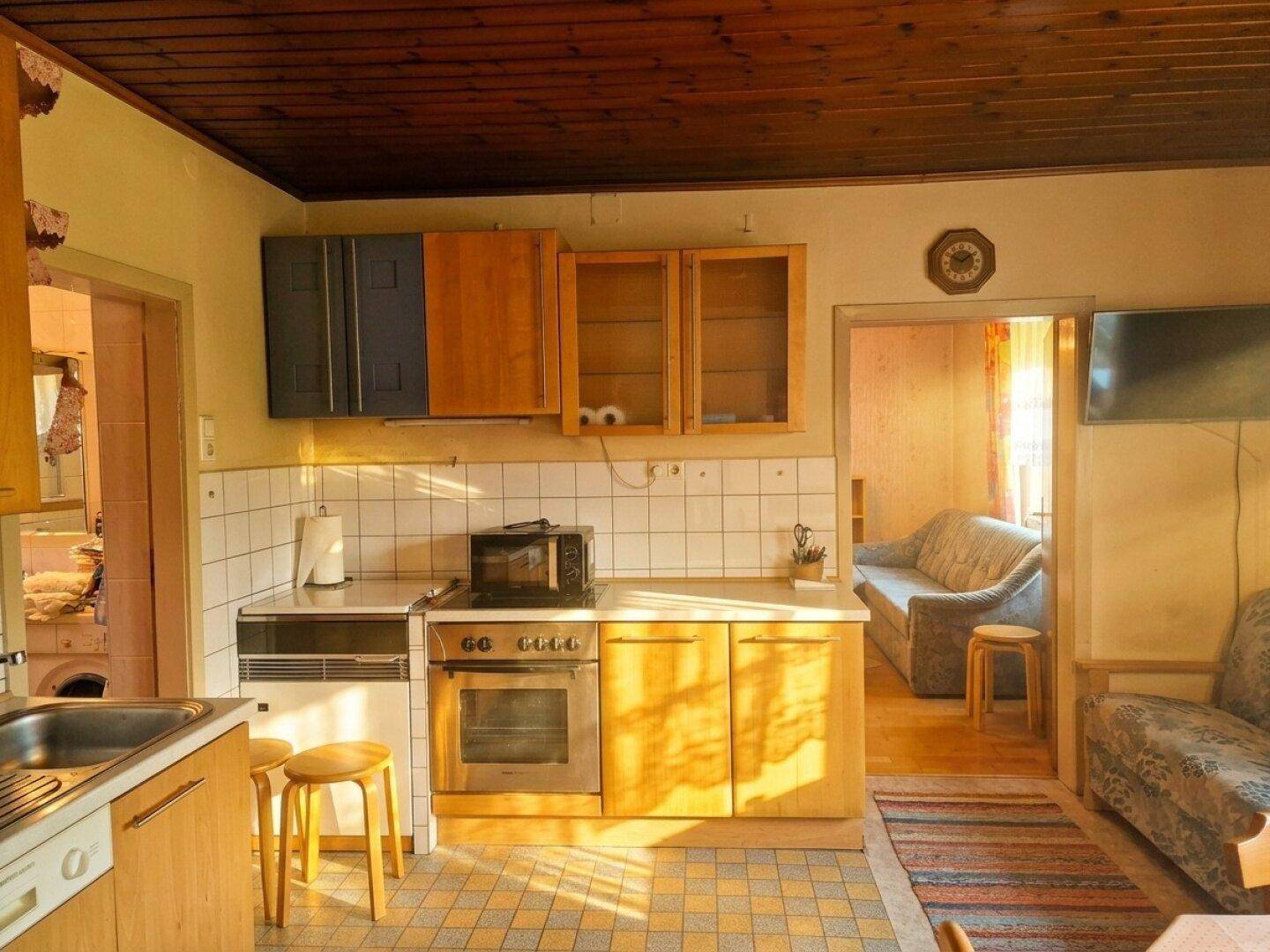 Funktionale Küche mit Holzschränken, Fliesenboden und Blick in den angrenzenden Wohnbereich.
