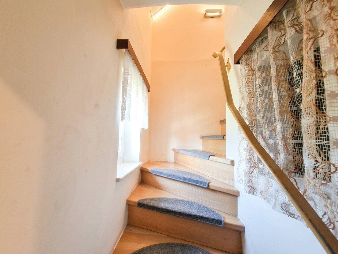 Holztreppe mit Teppichstufen und Fenster, führt in die obere Etage.