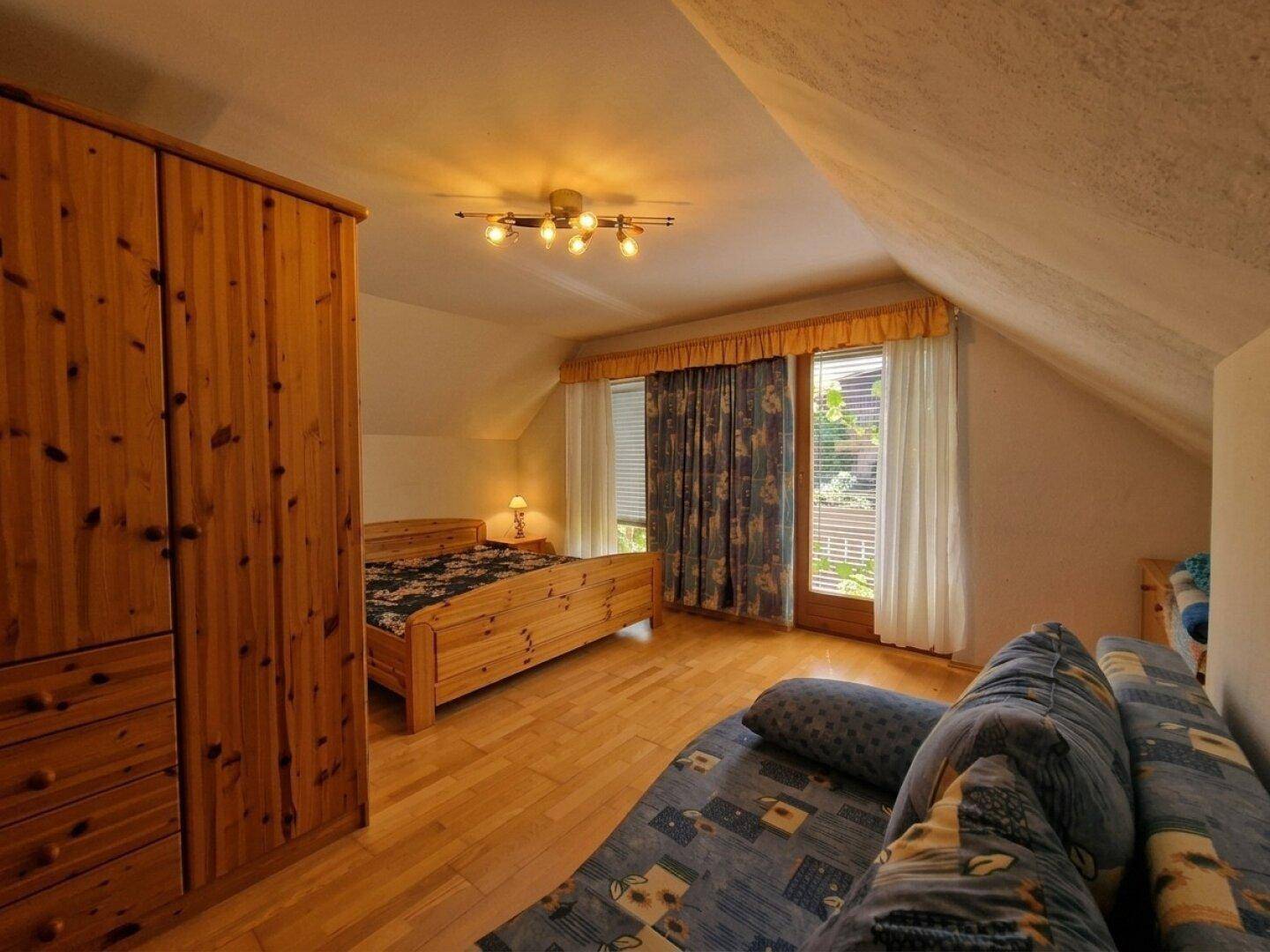 Helles Schlafzimmer im Dachgeschoss mit Holzboden, Bett und Zugang zum Balkon.
