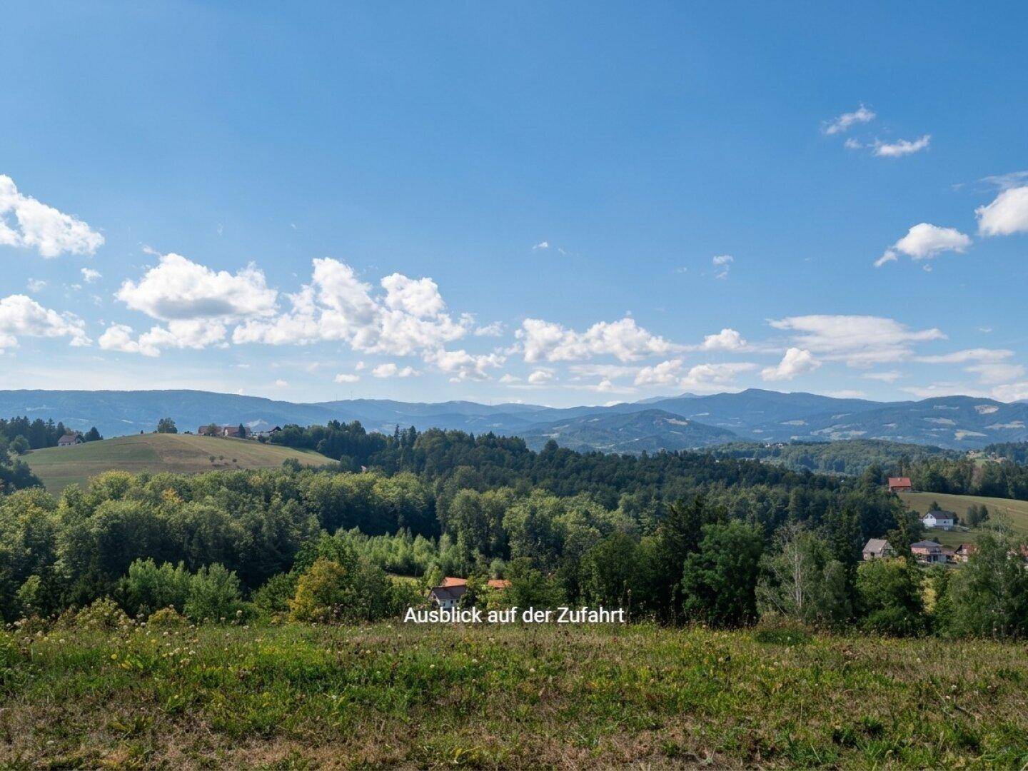 Panoramablick auf eine hügelige, bewaldete Landschaft mit vereinzelten Häusern in der Ferne.