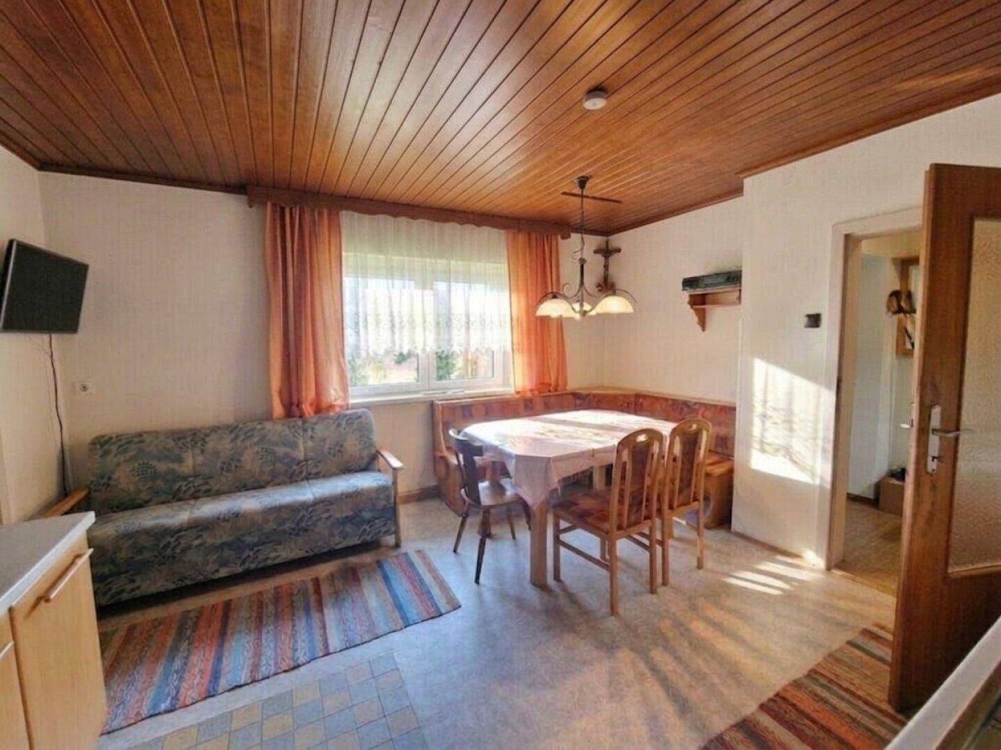Gemütlicher Wohn-Essbereich mit Holztäfelung an der Decke, Eckbank und Sofa.