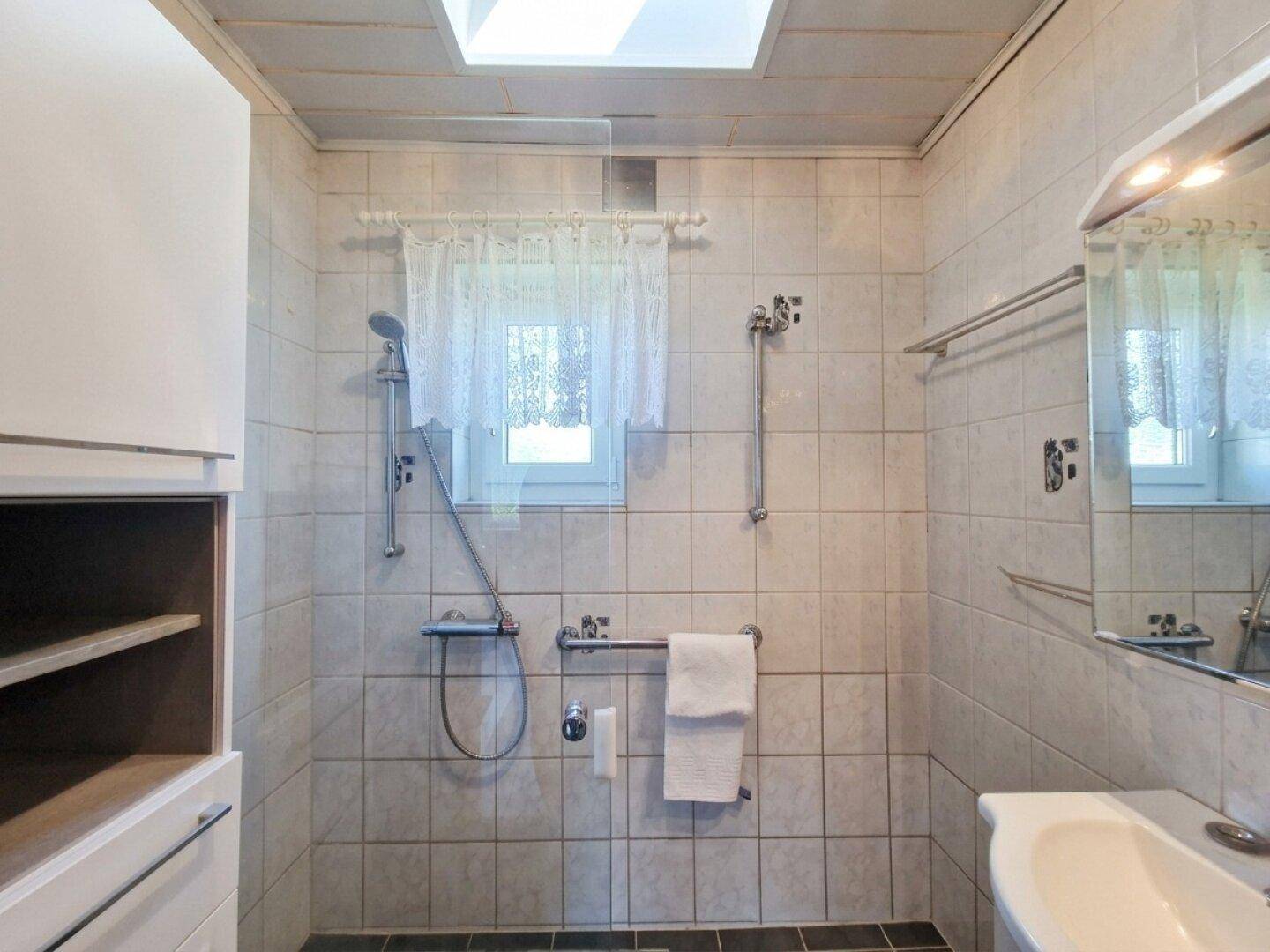 Gefliestes Badezimmer mit Dusche, Waschbecken und Fenster für Tageslicht.