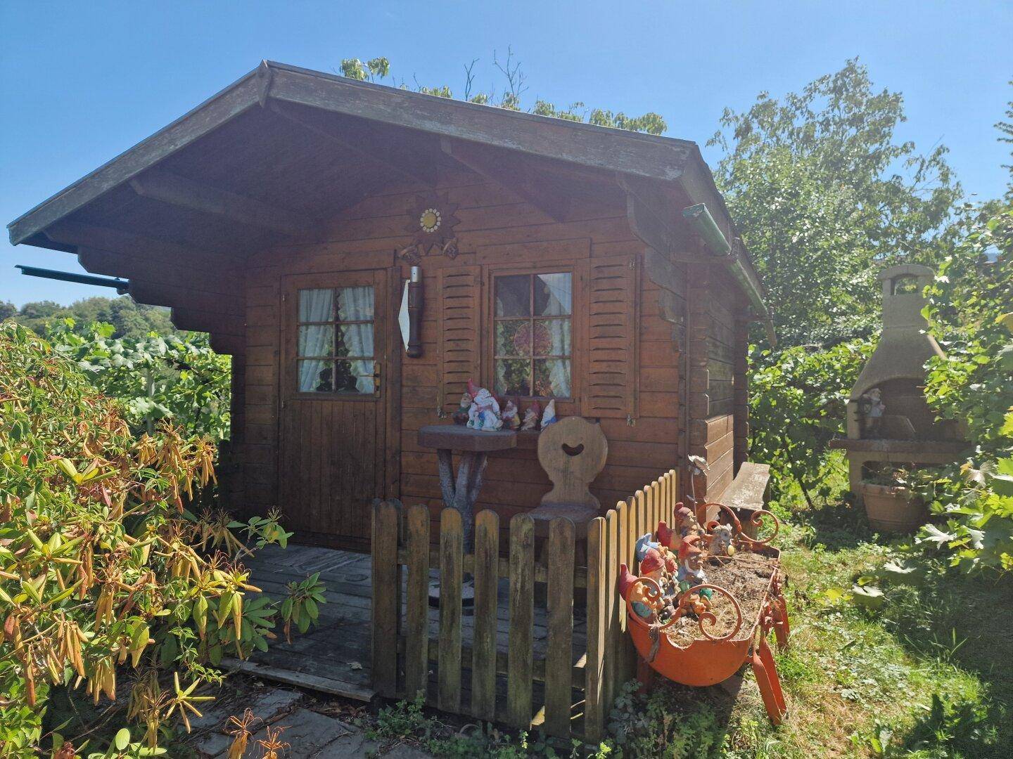 Kleine Holzhütte mit Sitzbereich, Gartenzwergen und einem Grill im Freien.