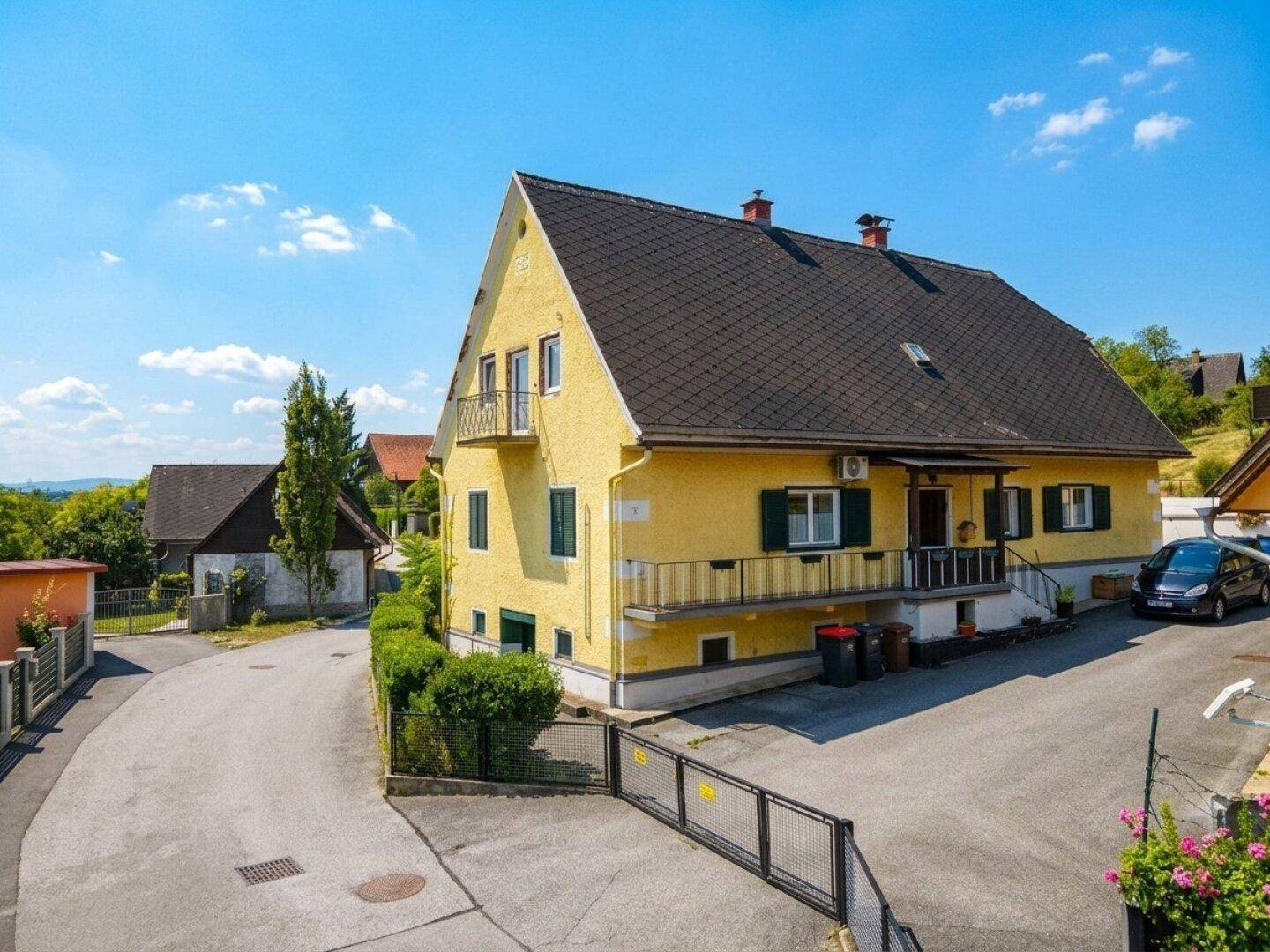 Gelbes Wohnhaus mit Satteldach, Balkonen und grünen Fensterläden in sonniger Umgebung.