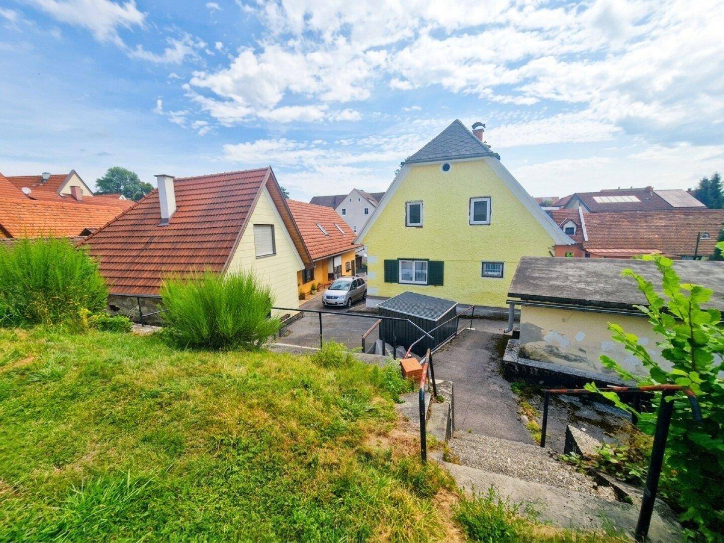 Ansicht des gelben Wohnhauses von einem erhöhten Gartenbereich mit Blick auf die Umgebung.