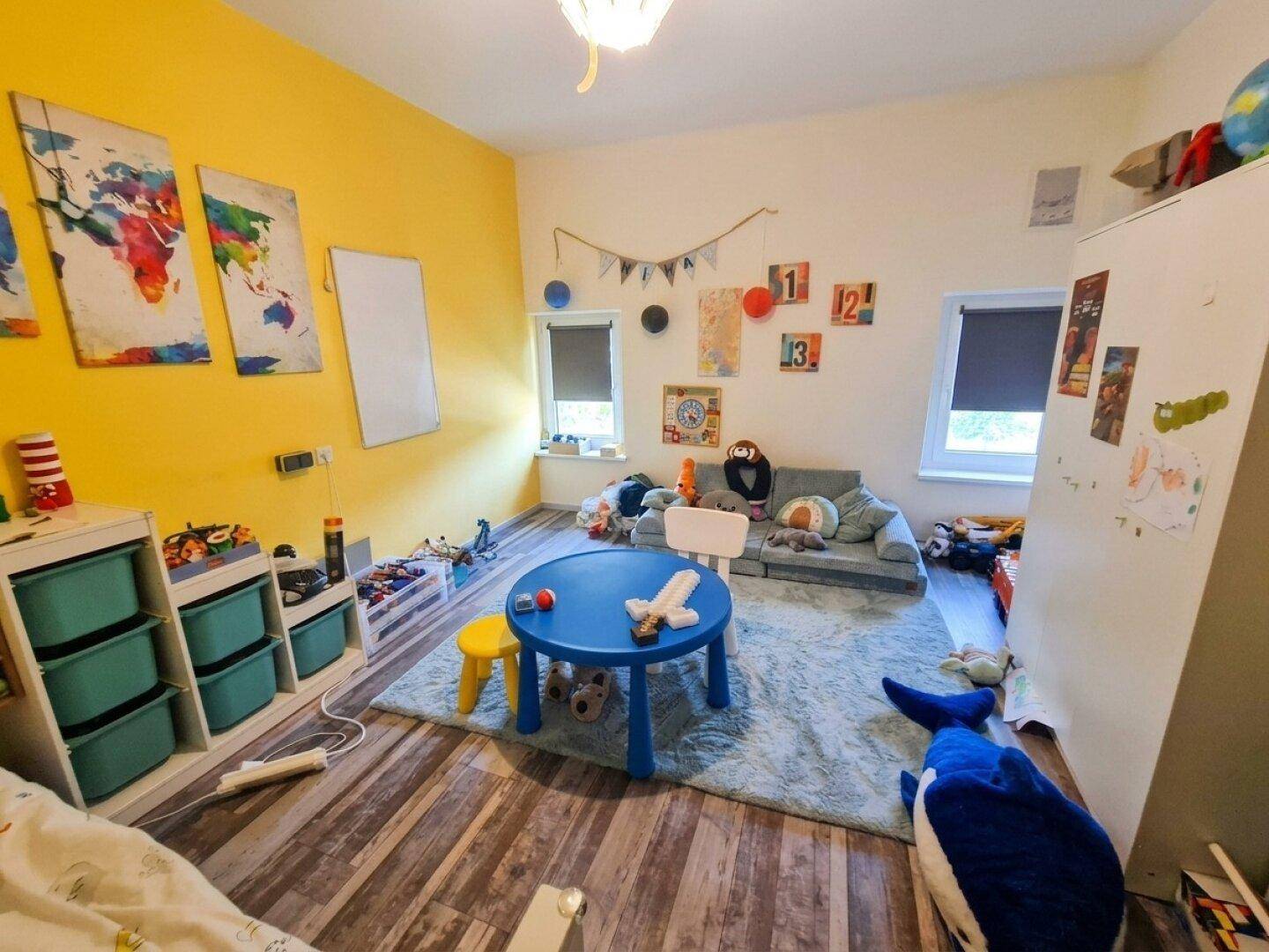 Helles Kinderzimmer mit gelber Wand, Spielbereich und bunten Dekorationselementen.