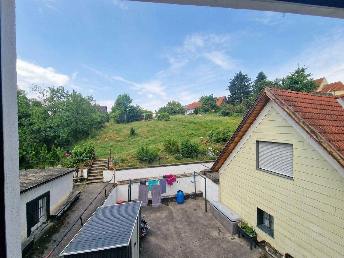Blick auf den Hinterhof mit Wäscheleine, Nebengebäuden und grünem Hang im Hintergrund.