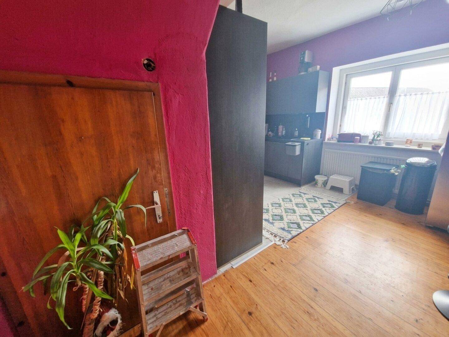Flur mit Holzboden und pinkfarbener Wand, der zu einem hellen Küchenbereich führt.